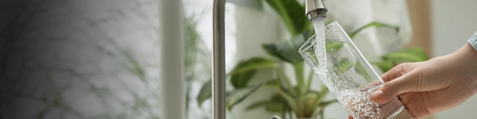 person pouring filtered water into a glass from a tap