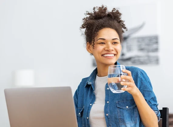 Woman drinking a glass of filtered tap water while on her laptop