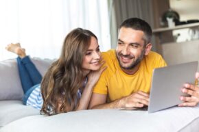 A woman and a man laying on the sofa looking at a laptop