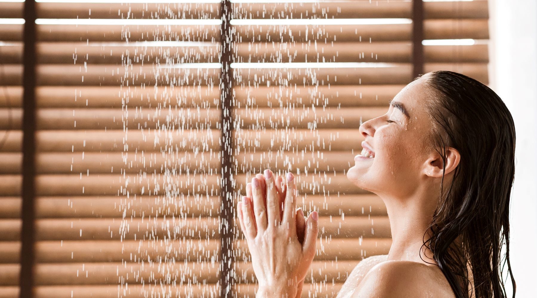 woman smiling in the shower in front of window blinds