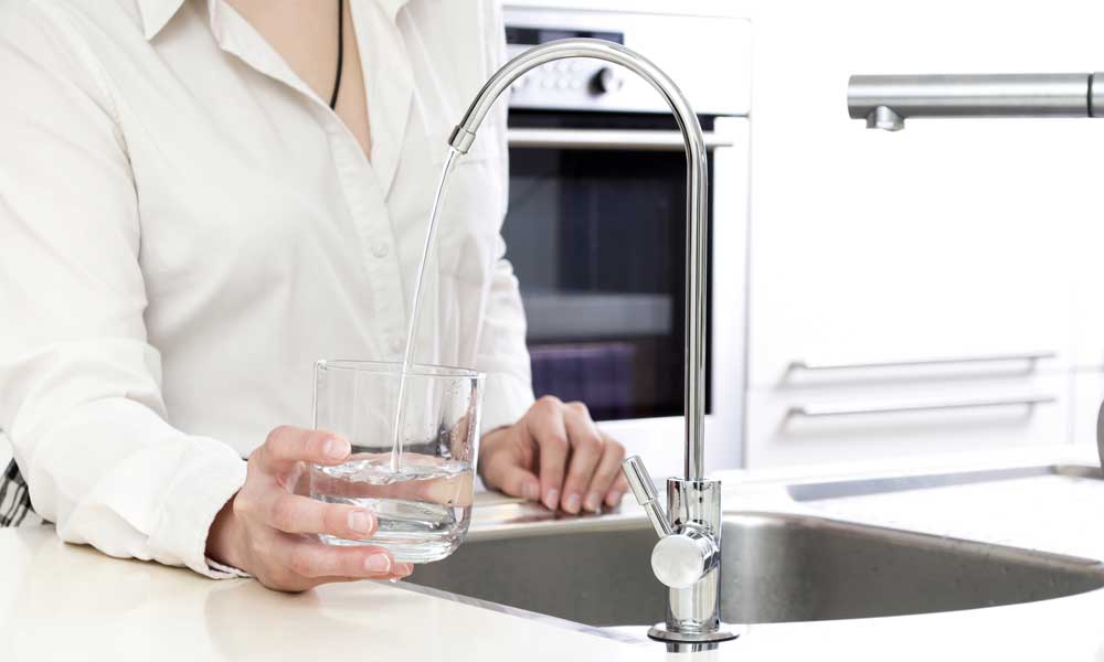 woman filling a glass with filtered water from a water filter tap