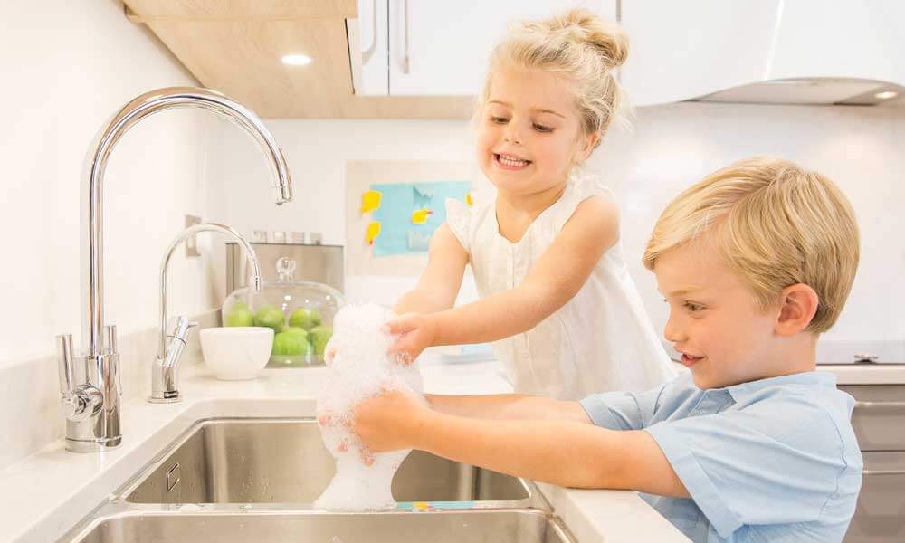 happy children washing their hands at a kitchen sink