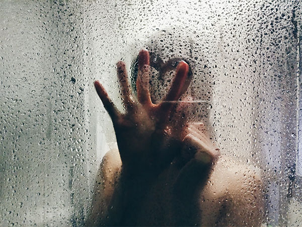 Hand on shower screen behind droplets