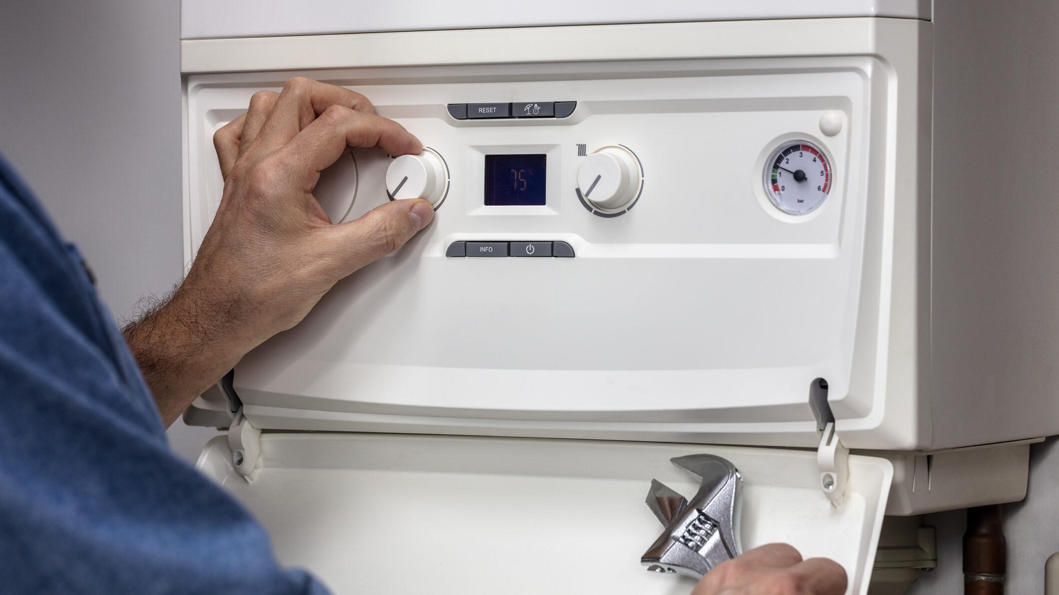 a hand turning the dial on a boiler with a spanner in the other hand